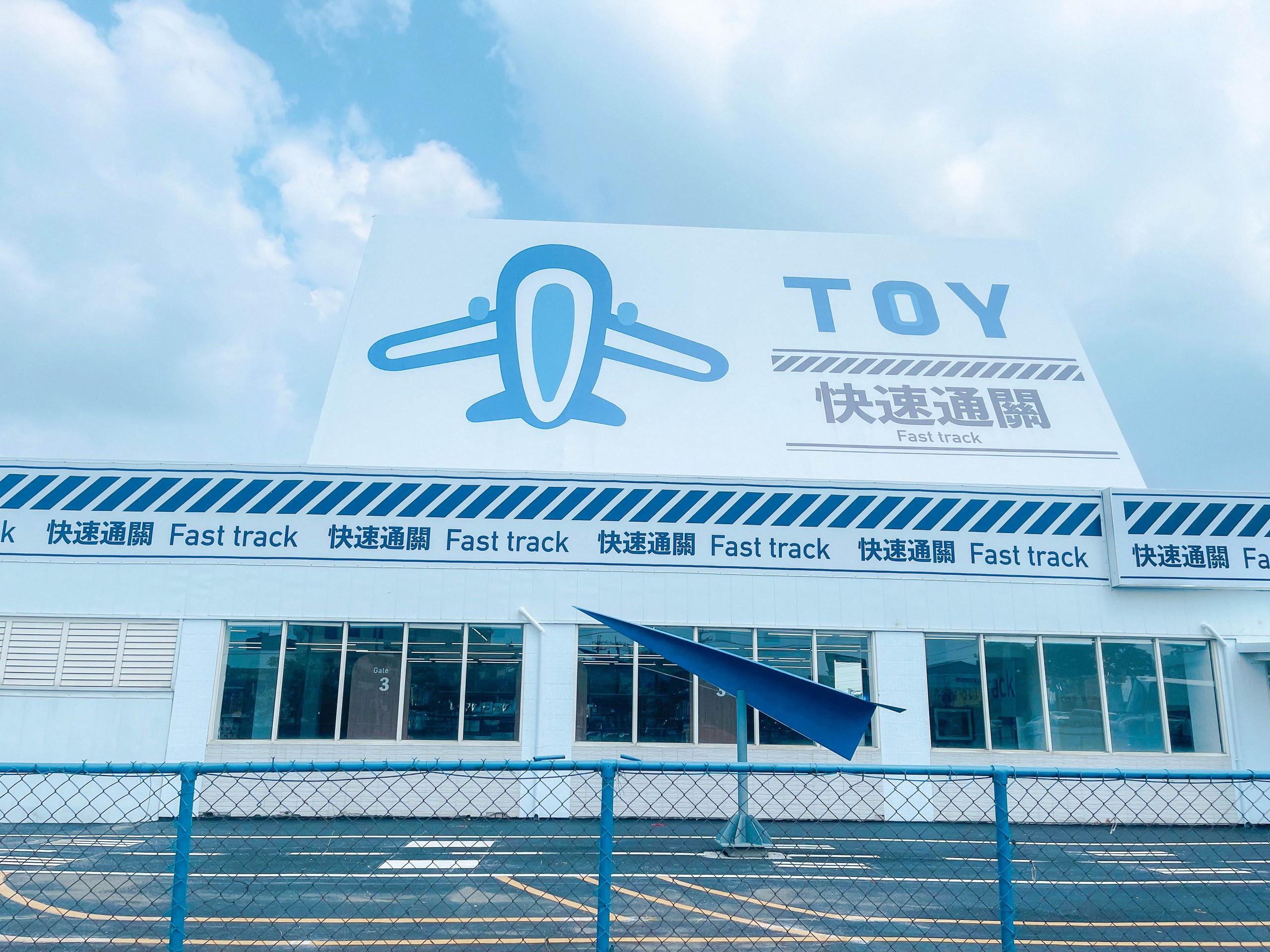 快速通關玩具店結帳區：藍色塑膠籃排在伸縮式滾輪輸送帶上，仿行李輸送帶，大面開窗引入自然光，動線清晰